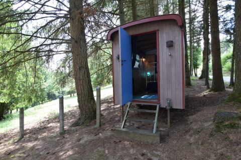 Et charmerende lille chalet ved navn 'Flons et Roulotte' i en skovklædt del af Belgien med åben dør.