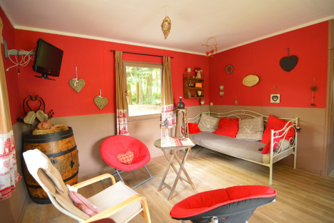 Hyggelig opholdsstue i chalet Flons et Roulotte i Belgien, med rød væg, sofa og dekorationer.