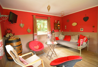 Hyggelig opholdsstue i chalet Flons et Roulotte i Belgien, med rød væg, sofa og dekorationer.