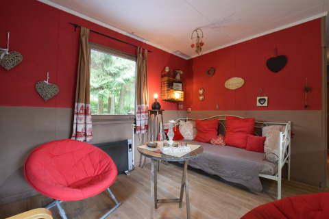 Hyggelig stue i chalet 'Flons et Roulotte' i Belgien med røde vægge, hjertepynt og moderne møbler.