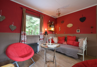 Hyggelig stue i chalet 'Flons et Roulotte' i Belgien med røde vægge, hjertepynt og moderne møbler.
