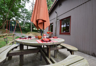 Udendørs spiseområde ved en træhytte i Flons et Roulotte, Belgien, med bord, parasol og gyngestativ.