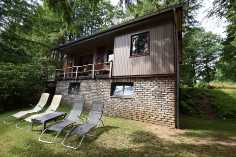 Chalet Flons et Roulotte i Belgien omgivet af skov, med fire liggestole på græsset foran huset.
