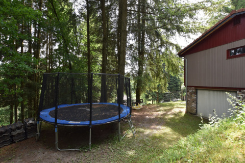 Skovklædt område ved chalet Flons et Roulotte i Belgien med trampolin og rødgråt hus om sommeren.