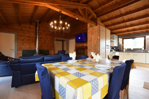 Knusse leefruimte in lodge Famenne, België, met houten plafond, blauwe zetels, eettafel en moderne keuken.