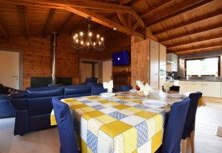 Knusse leefruimte in lodge Famenne, België, met houten plafond, blauwe zetels, eettafel en moderne keuken.