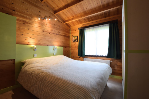 Slaapkamer met houten wanden en groene elementen in lodge 'Famenne', België, hoekzicht op het bed.