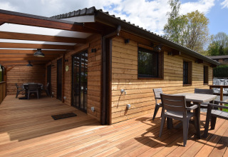 Houten terras met moderne stoelen en tafels bij lodge Famenne, midden in het groen in België.