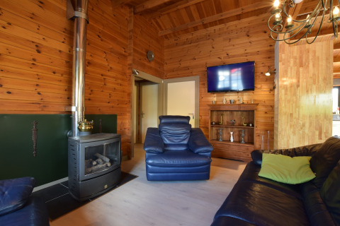 Woonkamer in lodge Famenne in België met houten wanden, zwarte kachel, lederen zetels en een tv.