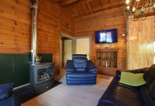 Woonkamer in lodge Famenne in België met houten wanden, zwarte kachel, lederen zetels en een tv.