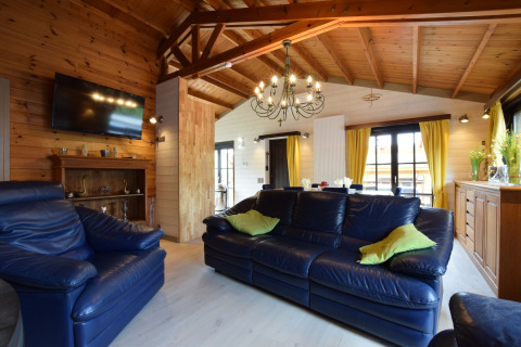 Woonkamer in lodge Famenne, België, met blauwe lederen zetels, houten plafond en gele gordijnen.