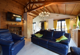 Woonkamer in lodge Famenne, België, met blauwe lederen zetels, houten plafond en gele gordijnen.