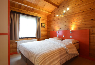 Houtbeklede slaapkamer met tweepersoonsbed en verlichting in het Famenne lodge, België.