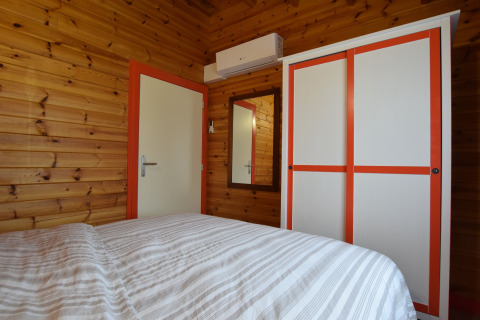 Slaapkamer met houten panelen, wit-oranje kast, spiegel en bed in lodge Famenne in België.