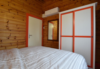 Slaapkamer met houten panelen, wit-oranje kast, spiegel en bed in lodge Famenne in België.