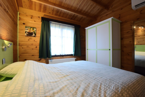 Slaapkamer van Famenne lodge in België met houten muren, dubbel bed, kast en raam met gordijnen.