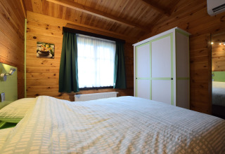 Slaapkamer van Famenne lodge in België met houten muren, dubbel bed, kast en raam met gordijnen.