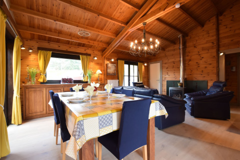 Het interieur van lodge Famenne in België met houten plafond, gele gordijnen, eetkamer en blauwe zetels.