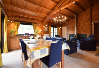 Het interieur van lodge Famenne in België met houten plafond, gele gordijnen, eetkamer en blauwe zetels.
