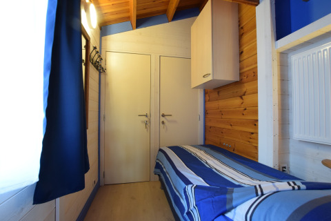 Kleine houten slaapkamer met een eenpersoonsbed en blauw bedlinnen in lodge Famenne, België.