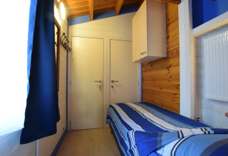 Kleine houten slaapkamer met een eenpersoonsbed en blauw bedlinnen in lodge Famenne, België.