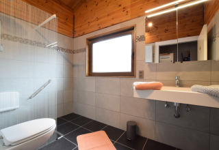 Moderne badkamer met houten plafond in lodge Famenne in België, voorzien van douche, wastafel en tegels.