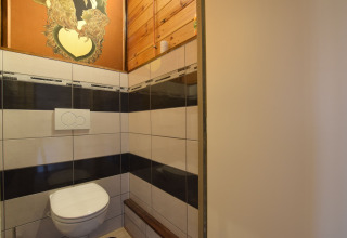 Moderne toiletruimte met zwevend toilet en kunstwerk bij Famenne-lodge in België, betegelde muren.