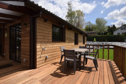 Houten terras met tuinmeubilair aan de lodge Famenne in België, omgeven door groen en bomen.