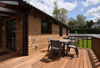 Houten terras met tuinmeubilair aan de lodge Famenne in België, omgeven door groen en bomen.