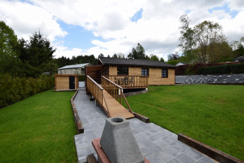 Houten chalet bij lodge Famenne in België met groene grasmat, houten oprit en bewolkte hemel.