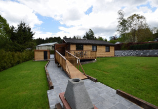 Houten chalet bij lodge Famenne in België met groene grasmat, houten oprit en bewolkte hemel.