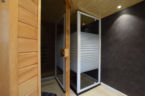 Binnenzicht van een sauna met houten deur en glazen wand in lodge Famenne in België.