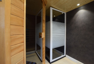 Binnenzicht van een sauna met houten deur en glazen wand in lodge Famenne in België.