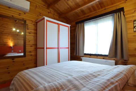 Knusse slaapkamer met houten muren, kast en raam in de lodge «Famenne» in België.