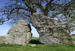 To storede sten stående ved siden af hinanden på en grøn mark ved et glamping-sted under en blå himmel.