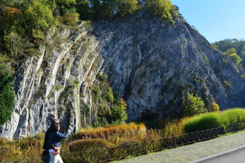 Person foran en stor klippe med lodrette linjer og grøn vegetation, taget ved et glampingområde.