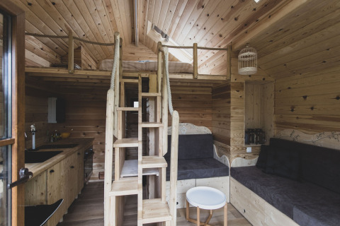 Interno della casa sull'albero 'Bird Nest' in Belgio con soppalco, scala e area salotto accogliente.