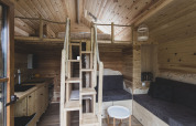 Interno della casa sull'albero 'Bird Nest' in Belgio con soppalco, scala e area salotto accogliente.