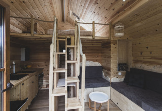 Interior of the 'Bird Nest' tree house in Belgium featuring a wooden loft, ladder and cozy seating.