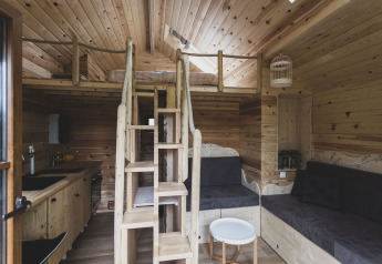 Interno della casa sull'albero 'Bird Nest' in Belgio con soppalco, scala e area salotto accogliente.