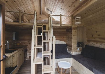 Interieur van boomhut 'Bird Nest' in België met houten slaapzolder, trap en knusse zithoek.