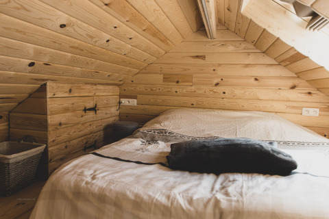 Cozy bedroom with slanted wooden walls and ceiling in the 'Bird Nest' tree house in Belgium.