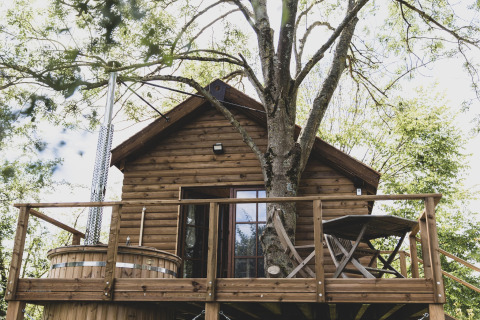 Treehouse called 'Bird Nest' in Belgium, featuring a wooden deck, hot tub, and outdoor furniture among trees.