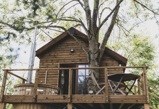Treehouse called 'Bird Nest' in Belgium, featuring a wooden deck, hot tub, and outdoor furniture among trees.