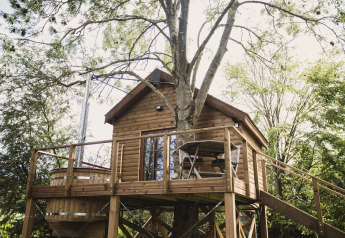 Baumhaus namens Bird Nest mit Holzterrasse, Sitzgruppe und Whirlpool im Grünen, aufgenommen in Belgien.