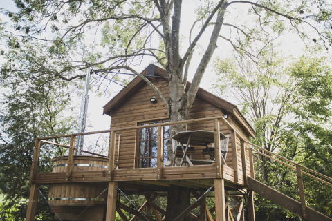 Casa sull’albero Bird Nest con terrazza di legno, tavolo, sedie e vasca idromassaggio in Belgio.
