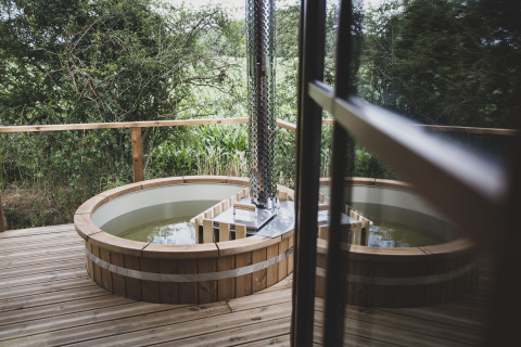Vasca idromassaggio esterna rotonda su terrazza in legno vicino alla casa sull'albero Bird Nest in Belgio.