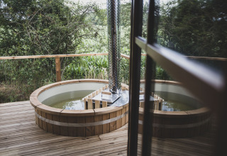 Vasca idromassaggio esterna rotonda su terrazza in legno vicino alla casa sull'albero Bird Nest in Belgio.