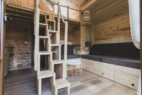 Interno della casetta sull’albero ‘Bird Nest’ in Belgio, con legno, divano e scale che portano al soppalco.
