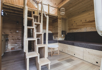 Interno della casetta sull’albero ‘Bird Nest’ in Belgio, con legno, divano e scale che portano al soppalco.